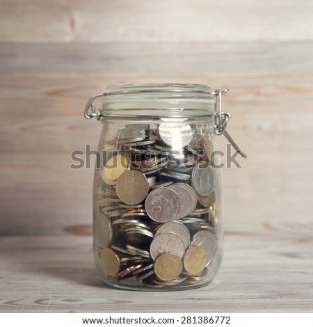 Coins in glass money jar, financial concept. Vintage wooden background with dramatic light.