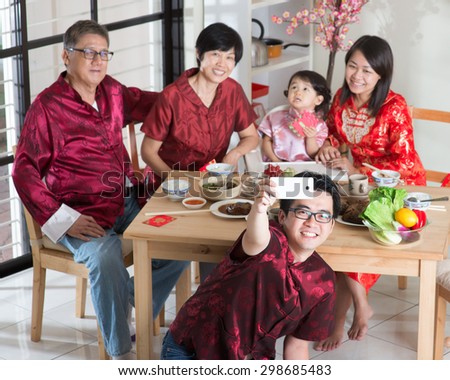 Chinese New Year, reunion dinner. Happy Asian Chinese multi generation family with red cheongsam selfie while dining at home.
