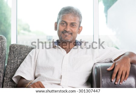 Portrait of mature Indian man sitting on sofa at home. Asian male relax on couch indoors.