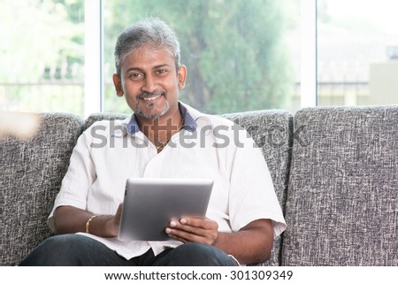 Modern technology. Mature Indian man using touch screen tablet computer at home. Asian people living lifestyle indoors.