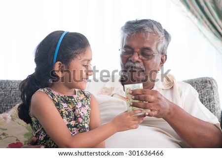 Portrait of Indian family at home. Grandchild giving a glass water to grandparent . Asian people living lifestyle. Grandfather and granddaughter.