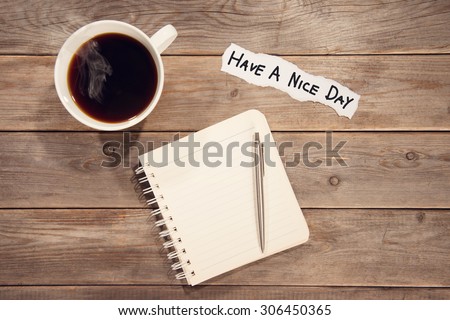 Top view work space with booklet, pen, cup of coffee and note message Have A Nice Day. Wooden table background in vintage toned.
