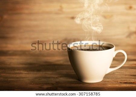 Steaming coffee in white cup in soft focus setting with dramatic ambient light, over dark wooden background.