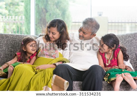 Happy Indian family at home. Asian parents bonding with their children, sitting on sofa. Adults and kids indoor lifestyle.