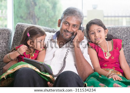 Daddy  making a phone call to mommy while taking care of children at home. Asian Indian family at home.