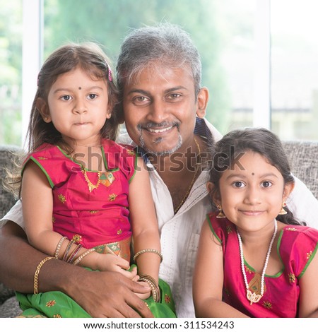 Happy Indian family at home. Asian father and daughters sitting on sofa smiling. Parent and children indoor lifestyle.