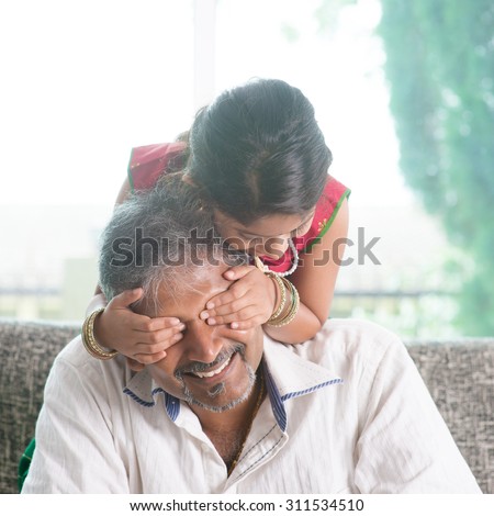 Happy Indian family at home. Asian girl surprising her father by covering daddy eyes. Parent and child indoor lifestyle.