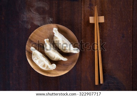 Top view fresh dumplings with hot steams on wood plate with chopsticks. Chinese meal on rustic old vintage wooden background.