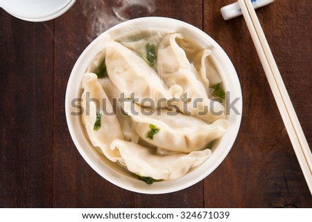 Top view fresh dumplings soup on plate with hot steams. Chinese meal on rustic old vintage wooden background.