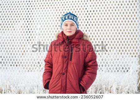 Boy standing in snow fence in a red jacket outdoors on a sunny foggy day looking at the camera