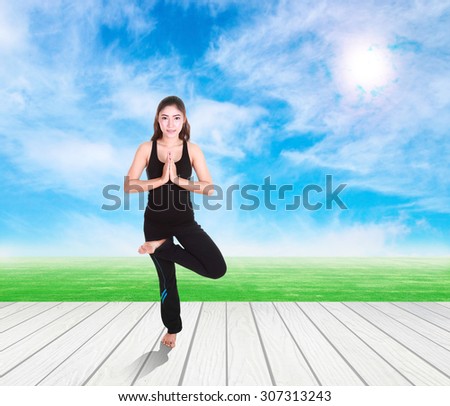 Young woman doing yoga exercise on wood floor with green grass and sky