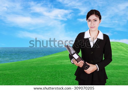 business woman holding folder documents with green grass field and sea background