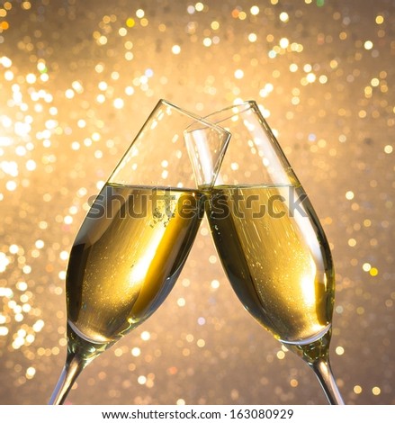 champagne flutes with golden bubbles make cheers on light bokeh background