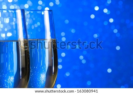pair of a champagne flutes make cheers on blue light bokeh background with space for text