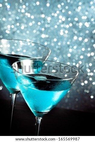 a pair of glasses of fresh blue cocktail with ice on blue tint light bokeh background on bar table