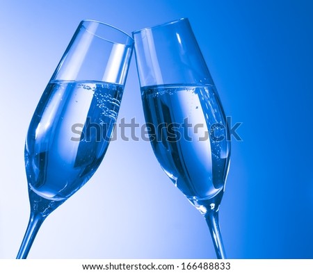 a pair of champagne flutes with bubbles being clinked together on blue background with space for text