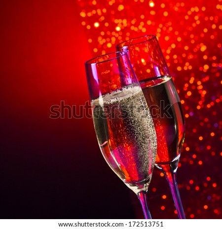 champagne flutes with golden bubbles on dark red and violet light bokeh background with space for text