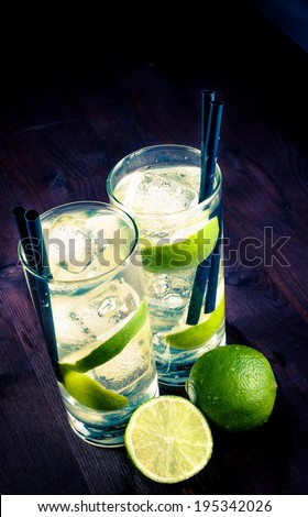 two glasses with cocktail and ice with lime slice on wood background, disco club atmosphere