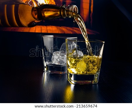 man pouring glasses of whiskey with ice cubes in front of the fireplace at night