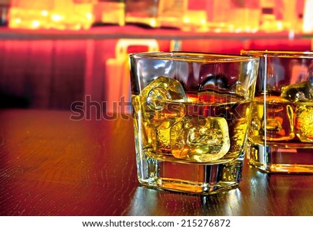 glasses of whiskey with ice on bar table near whiskey bottle on warm atmosphere lounge bar concept