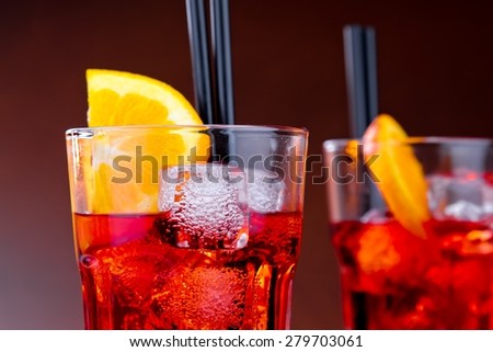 close-up of two glasses of spritz aperitif aperol cocktail with orange slices and ice cubes on colored gradient background