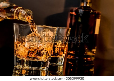 barman pouring whiskey in front of whiskey glass and bottles on black table with reflection