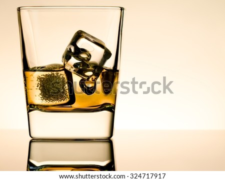 one glass of whiskey with ice cubes on table with reflection, light brown atmosphere, time of relax with whisky