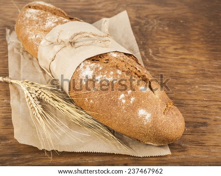 long loaf in paper packaging with ears of wheat on the wooden background