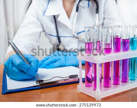 doctor writes beside test tubes standing on a light background