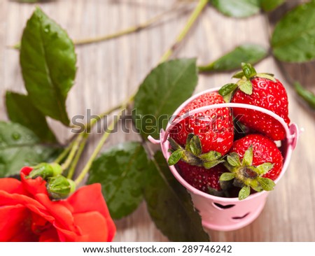 bucket of strawberries and rose on a wooden background