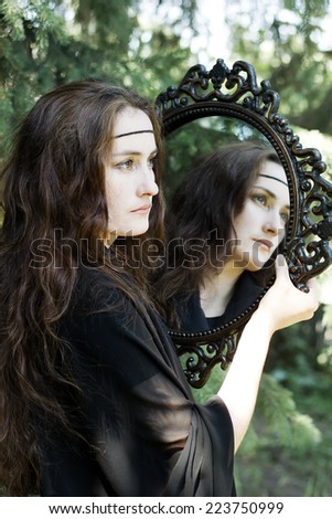 Beautiful witch in black dress with old mirror