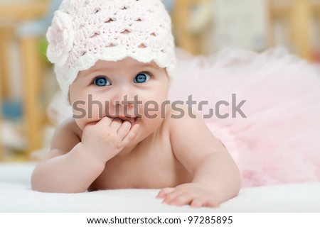 Charming child. Little girl with hat lying on her stomach and sucks fingers