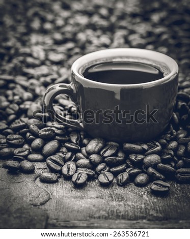 Closeup of dark roasted coffee beans and a cup filled with fresh hot coffee. Food and drink backdrop showing aromatic and beautiful coffee beans.