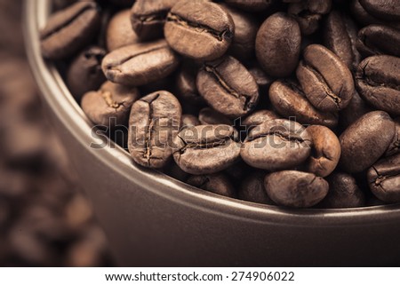 Closeup of dark roasted coffee beans in a cup viewed from above. Food and drink backdrop showing aromatic and beautiful coffee beans. Can be used as a conceptual image for breakfast time.