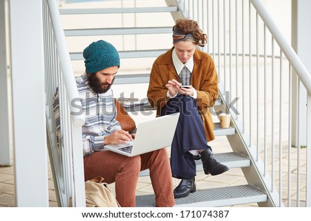 Hipster couple using computer and smartphone at university campus