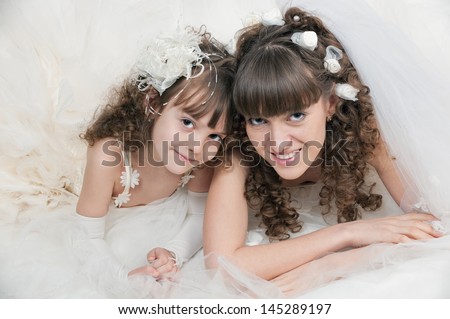 Portrait of a sensual young mother and daughter in a beautiful wedding dress posing in studio on white
