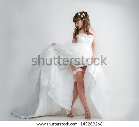 Photo in full height leggy elegant model in a beautiful wedding dress posing in studio