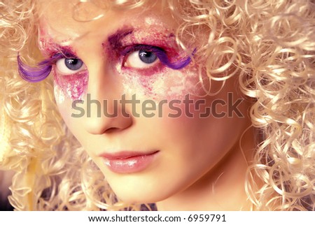 girl like a doll with curly blond hair and extravagant make-up with extra long lashes