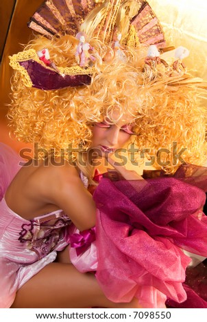 girl like a doll with curly blonde hair and extravagant make-up in medieval clothes with disguise in her hand