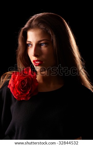 portrait of a young beautiful brunettes with red lips in a black blouse decorated with a rose