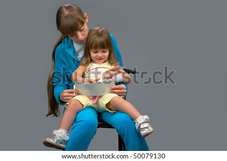 a young girl in a blue suit sitting with a child in her arms and teaches her to read