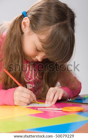 close-up of a beautiful little girl in a pink blouse draws on colored paper