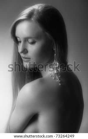 Black and white photo of pretty young sexy naked woman with nice jeweller decor on a grey background