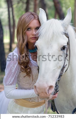 Portrait of a glamour young woman with wavy long hairs in refined white clothing and beautiful horse somewhere in a park