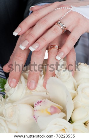 Photo of two tender hands of the groom and the bride with wedding rings and bouquet of white roses close up