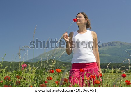 Beautiful young woman smelling a flower enjoying a perfect sunny day in the countryside