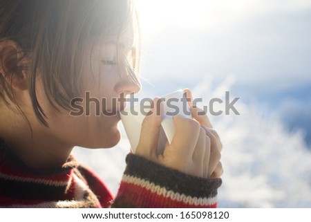 Beautiful young woman drinking hot drink outside on a sunny cold winter morning