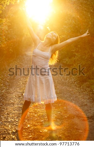Beautiful young girl dancing in the golden light of the setting sun on forest track