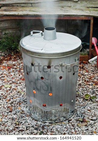Garden incinerator bin burning garden waste with smoke coming out of the flue