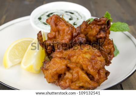 Onion Bhajis & Mint Raita - Deep fried south asian snack yoghurt and mint dip, garnished with mint leaves and lemon wedges on a white plate.